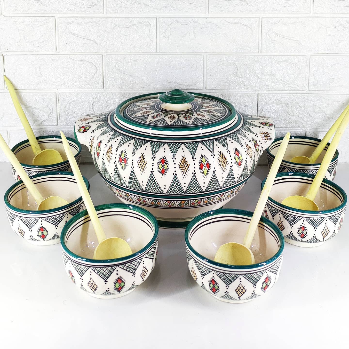 Ensemble de soupière Ramadan en porcelaine blanche avec bord doré, 12 bols assortis et 6 sets de table blancs avec motif floral vert et doré. La table est dressée pour un repas de Ramadan.