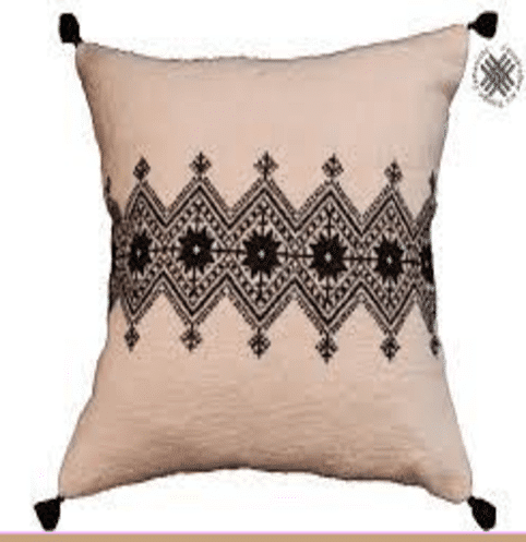 Un coussin décoratif avec un motif de cercles noir et blanc, accompagné d'un bol et d'une cuillère, avec une tasse sur une table à proximité